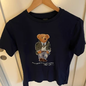 Mörkblå Polo Bear t-shirt från Ralph Lauren - Mörkblå t-shirt från Polo Ralph Lauren med ikoniskt Polo Bear-tryck på bröstet. Storlek 12 år