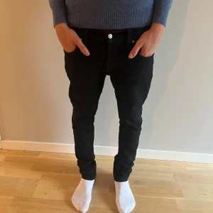  Nudie Jeans - Snygga svarta jeans från Nudie Jeans. De har klassisk femficksdesign, svarta sömmar och en diskret logga på bakfickan. Jeansen är tillverkade i stretchigt bomullsmaterial för en bekväm och slim passform. Perfekta för dig som gillar stilrena och moderna jeans.