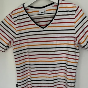 Randig Multifärgad T-Shirt - Säljer denna multifärgade randiga t-shirten med V-ringning. Den är använd men i mycket fint skick. Står storlek 40 på lappen men passar snarare en XS/S. Bredd: 39 cm / Längd: 55 cm