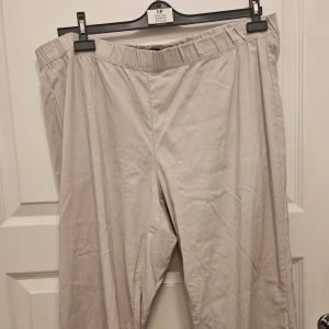 Stretchig byxa från Zhenzi i storlek 50/52 - Stretchig capribyxa i en ljusbeige nyans från Zhenzi. Byxorna har resår i midjan och litet sprund samt lite strass i bensluten. I gott använt skick  Storlek 50/52 Längd 81 cm Midjebredd 120 cm