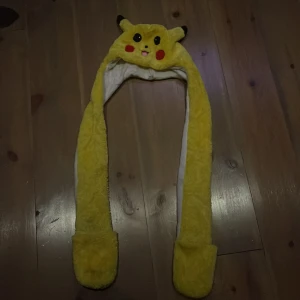 Gul Pikachu mössa med långa öron - Supermjuk och fluffig mössa som föreställer Pikachu från Pokémon. Mössan är gul med svarta och röda detaljer, har långa öron och fickor för händerna längst ner. Perfekt för dig som vill sticka ut och hålla dig varm under kalla dagar.