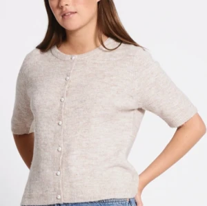 Beige kofta med pärlknappar - Supersöt beige kofta med korta ärmar och pärlknappar framtill. Mjuk och stickad känsla, perfekt till jeans eller kjol. Enkel och stilren design som passar året runt. Kom dm vid frågor