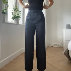 Mörkblå vida kostymbyxor - Snygga mörkblå kostymbyxor med hög midja och vida ben. Byxorna har pressveck, hällor för bälte och dold dragkedja. Byxorna är storlek 38/M men passar mer storlek 36/S. Använda 2 gånger, mycket fint skick