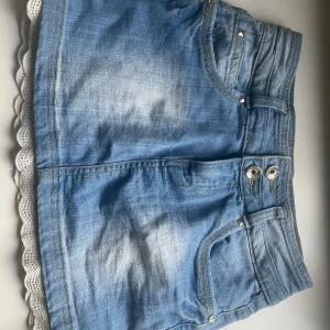 Ljusblå jeanskjol med spetskant - Söt ljusblå jeanskjol med två knappar framtill, klassiska fickor och en vit spetskant längst ner. 