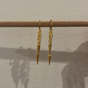 Guldiga örhängen med kedja och spikes - Snygga örhängen i guldton med kedjedetalj och två spetsiga spikes som hänger ner. Ger en edgy vibe och passar perfekt om du vill sticka ut. Lätta att bära och riktigt coola till både streetwear och mer dressade outfits.