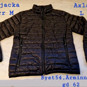 Svart pufferjacka herr M - Svart pufferjacka från Hampton Republic enl AI sök( min man klippt bort etikett) i storlek M. Jackan har horisontella quiltade sömmar, hög krage och två dragkedjeförsedda fickor. Tillverkad i syntetmaterial och perfekt för kyliga dagar. Enkel och stilren design med diskret logga på bröstet.