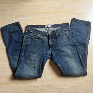 Acne jeans - Säljer ett par klassiska blå jeans från Acne med raka ben och snyggt slitna detaljer. Jeansen har fem fickor, gylf med dragkedja och knapp, samt kontrastsömmar. Perfekta för dig som gillar en tidlös och avslappnad look.