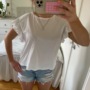Vit T-shirt  med volangärmar - Supersöt vit T-shirt med volangdetaljer på ärmarna och rund halsringning. Modellen är lite lös och luftig, perfekt för varma dagar. Tillverkad i mjuk bomull som känns skön mot huden. Enkel att styla med både jeans och kjol för en fräsch look. Tröjan är ifrån Zara och säljer för 65kr❣️i nyskick ❣️storlek M men passar mer som en S. Säljer även samma tröja fast i blå!💙