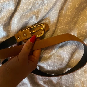 Brunt skärp med guldfärgat spänne - Snyggt brunt bälte med ett stilrent guldfärgat spänne. Bältet är i klassisk design och passar perfekt till jeans eller byxor. Insidan är svart och materialet känns stabilt och mjukt. Perfekt accessoar för att lyfta din outfit.