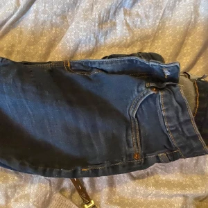 Blå jeans med klassisk passform - Säljer ett par blå jeans med klassisk femficksdesign och kontrastsömmar. Jeansen har normal midja och raka ben, perfekta för en avslappnad stil. Materialet är slitstarkt denim i bomull.
