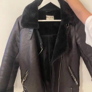 Svart teddyjacka från NA-KD, stl 32 - Snygg svart teddyjacka från NA-KD med stora slag, dragkedjor och mjukt foder. Jackan har en cool bikerstil med detaljer i silver och är perfekt för kalla dagar. Oversized känsla och riktigt mysig att bära.