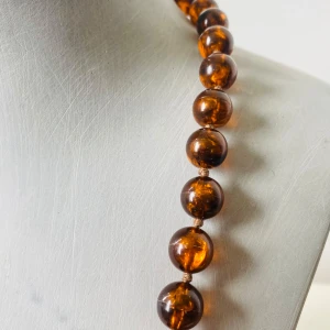 Brunt bärnstensset halsband & örhängen - Snyggt set med halsband och clip-on örhängen i brun bärnsten-look. Halsbandet har stora, runda pärlor i transparent bärnstensfärg och örhängena är halvmåneformade med metallclips. Perfekt för dig som gillar retrovibbar och statement-smycken.