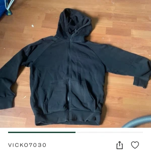 Svart hoodie från Peak Performance - Svart hoodie från Peak Performance med broderad logga på bröstet. Tröjan har dragkedja hela vägen, två fickor fram och en skön huva. Perfekt för chill dagar eller när du vill ha en clean streetstyle-look.