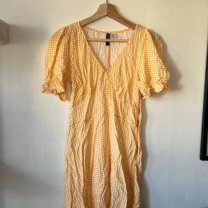 Gul- och vitrutigt omlottklänning från H&M Divided - Söt gul- och vitrutigt klänning från H&M Divided med v-ringning och korta puffärmar med volangkant. 