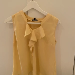 Gul blus volang från Stockh LM💛 - Snygg gul blus från Stockh LM i storlek 36. Ärmlös modell med volangdetalj framtill som ger en cool och feminin touch. Lätt och luftig, passar perfekt till varmare dagar☀️