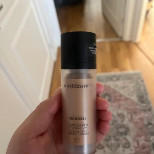 bareMinerals Liquid Mineral Foundation - Flytande foundation från bareMinerals i originalserien. Kommer i en stilren, frostad plastflaska med svart lock. Ger en naturlig finish och innehåller SPF 20. Perfekt för dig som vill ha en lätt och fräsch bas med mineralingredienser.