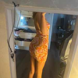 Klänning  - Säljer en superfin kort klänning med swirlmönster i orange, rosa, gul och vit. Klänningen är ärmlös med halterneck och öppen rygg, perfekt för sommarens alla tillfällen. 