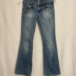 -VINTAGE-  Diesel bootcut ljusblå - Snygga bootcut jeans i ljusblå denim med slitna detaljer framtill och bakfickor. Klassisk femficksmodell med dragkedja och knapp. Jeansen har en lätt utsvängd passform nertill och coola slitningar för en trendig look VÄLDIGT VINTEGE~20år , Orginella Storlek 12 passar 23/30 tjej , öppet hål i botten men syns ej och kan sys upp