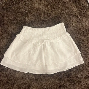 Vit volangkjol från Gina Tricot - Supersöt vit kortkjol från Gina Tricot med smockad midja och dubbla volanger. Kjolen är lätt och luftig, perfekt för varma dagar. Den har en flowy känsla och passar dig som gillar en feminin och trendig stil. Den är i storlek 170 men jag tycker den är väldigt liten i storleken så skulle sitta perfekt på 164 skulle jag säga. Men gillar man korta volangkjolar så är denna perfekt för storlek 170.