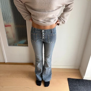Blå bootcut jeans med detaljer  - Pris kan diskuteras!! Säljer ett par blå bootcut jeans från Yi Jue med coola framfickor dekorerade med nitar och knappar. Jeansen har låg midja, smala ben upptill och utsvängda nertill. Jättestretchiga, jag har storlek 36 om de sitter perfekt på mig.