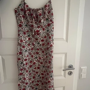 Blommig långklänning med knyt - Superfin långklänning med smala axelband och blommigt mönster. Klänningen har knytning framtill, smock i ryggen och dragkedja i sidan. Perfekt för sommarens alla tillfällen.