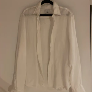 Vit skjorta från Black i silke - Stilren vit skjorta från Black i tunt, lyxigt silke. Klassisk krage, långärmad och med knappar framtill. Perfekt för dig som gillar en clean och tidlös look. Skjortan har en lätt glansig finish och känns riktigt skön mot huden.