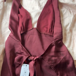 Vinröd halterneckklänning med knyt - Vinröd halterneckklänning med djup v-ringning och knyt i ryggen. Perfekt för dig som vill sticka ut med en elegant och trendig look. Nypris 400