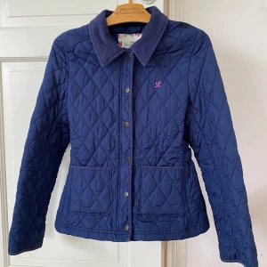 Quiltad blå jacka från H&M L.O.G.G. - Quiltad marinblå jacka från H&M L.O.G.G. med klassisk krage i bomull, tryckknappar framtill och två stora fickor. Jackan har ett diskret broderat L på bröstet och är helfodrad. Perfekt för dig som gillar stilren och tidlös look.