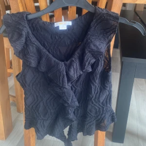 Svart volangblus från Gina Tricot -  svart blus från Gina Tricot med volangdetaljer längs halsringningen och nederkanten. 