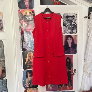 Pat Perkins’s 60-tals klänning  - Jättefin röd 60-tals klänning, med knappar och fejk fickor framtill. I fint skick. Storlek saknas, uppskattar den till en L. Jag kan mötas upp i Uddevalla centrum, annars fraktar jag gärna. Köparen står för frakten. (Står ej för postens slarv) katt finns i hemmet. 