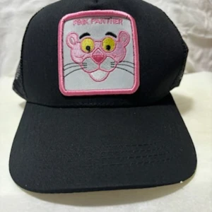 Svart Pink Panther keps med mesh - Cool svart keps med broderad Pink Panther-figur framtill i rosa och gult. Kepsen har mesh på sidorna och baktill för extra ventilation samt en rosa tassdetalj på sidan. Justerbar snapback för perfekt passform. Perfekt för dig som gillar statement-plagg!