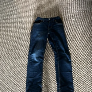 Levi's 512 mörkblå jeans slim fit - Snygga Levi's 512 jeans i mörkblå tvätt med klassiska kontrastsömmar och fem fickor. Modellen är slim fit och sitter tajt men bekvämt längs benen. Jeansen har knapp och dragkedja framtill samt Levi's ikoniska läderpatch bak. Passar folk som är 145cm- 160cm