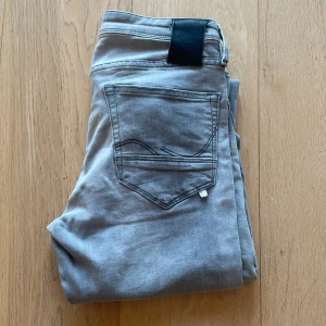 Jack n Jones glenn/slim - Snygga grå jeansbyxor i rak passform med klassiska fem fickor och svarta detaljer på bakfickan. Byxorna har normal midja och är tillverkade i mjukt bomullsmaterial med lite stretch för extra komfort. Knappt använda.