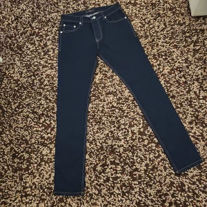 Mörkblå skinny jeans från Lacoste - Snygga mörkblå jeans från Lacoste med kontrastsömmar och klassisk femficksdesign. Byxorna har skinny passform och är tillverkade i jeansmaterial. Bakfickorna har Lacoste-logga och läderpatch i midjan. Perfekta för en clean och stilren look.