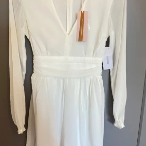 Vit kortklänning Dahlia Dress - Superfin vit kortklänning från Bubbelroom som är helt oanvänd! Passar perfekt nu till studenten eller sommaren! Finns ett band runt midjan som gör att knyta både fram och bak😍 Inköpt för 599. Köparen står för frakten💞☀️