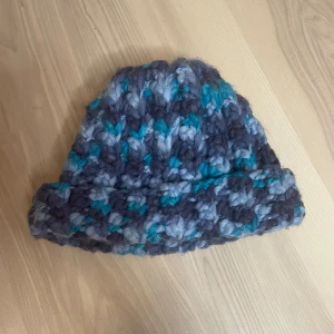 Handvirkad mössa i blå och grå toner - En mysig, Handvirkad mössa i tjockt garn med blå, turkosa och grå nyanser. Mössan kan man ha rak eller vika så den får en kant 