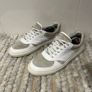 Jacob Cohën Skor -  Snygga och exklusiva sneakers från Jacob Cohën i vit och ljusgrå färgkombination. Ovandelen är en mix av läder och mocka, vilket ger en stilren och lyxig känsla. Skorna är sparsamt använda och i mycket fint skick, med fräscha sulor och minimala tecken på slitage.  Passar perfekt både till jeans och chinos – ett utmärkt val för dig som gillar stilrena premiumskor.  🔹 Storlek: 43 🔹 Färg: Vit / Ljusgrå 🔹 Material: Läder och mocka 🔹 Skick: Mycket fint skick, sparsamt använda  ⸻  