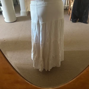 Brandy melville kjol - Säljer en vit långkjol med flera volangpartier. Kjolen har en mjuk och flowy känsla, perfekt för varmare dagar. Resår i midjan för bekväm passform.