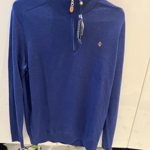 Blå merinoulltröja med dragkedja från Morris - Snygg blå långärmad tröja från Morris i 100% merinoull. Tröjan har en liten dragkedja vid halsen och en broderad logga på bröstet. Perfekt för dig som gillar klassisk och stilren design.