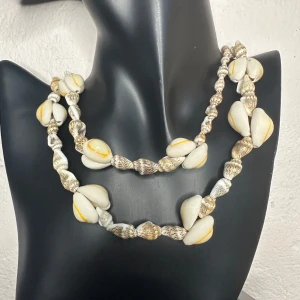 Vintage snäckhalsband – Retrofynd direkt från 70-talet för strandinspirerad bohostil - Vintage snäckhalsband från 70-/80-talet med handpolerade natursnäckor i olika former. Ca 90 cm långt, snäckor ca 0,5–1,5 cm. Kan bäras långt eller dubbelträtt. Vackert skick med naturlig glans – perfekt för dig som gillar strandstil, boho eller retroaccessoarer. Prutning ej möjlig, men jag ger rabatt vid köp av flera saker. Rensar smyckesskrin – kika gärna på mina andra annonser också!