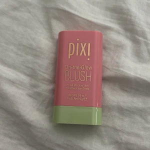 Pixi On-the-Glow Blush stick - Krämrouge i stickformat från Pixi i färgen 'Fleur'. Kommer i en rosa och ljusgrön förpackning. Enkel att applicera direkt på kinder och läppar för en fräsch, återfuktande finish. Perfekt att ha med i väskan för touch-ups under dagen.