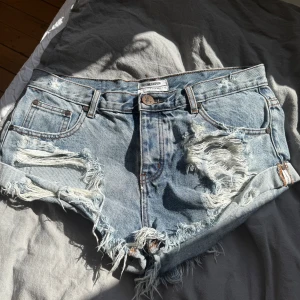 Ljusblå slitna jeansshorts från One Teaspoon - Säljer ett par ljusblå jeansshorts från One Teaspoon med låg midja, slitna detaljer och fransig kant. Storleken står 29 men sitter som S/M