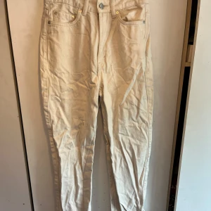 Beige jeansbyxor från Rowe - Säljer ett par beige jeansbyxor från Rowe med klassisk femficksdesign och raka ben. Byxorna har normal passform och stängs med dragkedja och knapp. Perfekta till många olika outfits! Tyvärr lite noppriga och fått en fläck (se bild 2&3)