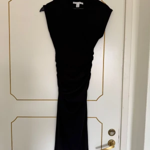 Svart långklänning från Amisu - Säljer en svart långklänning från Amisu med enkel och stilren design. Klänningen har ärmlös modell och smickrande drapering längs midjan. Perfekt för dig som gillar minimalistisk stil.