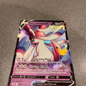 Dark Sylveon V - Samlarkort med Dark Sylveon V från Pokémon-serien. Kortet har färgstark design och coola attacker som Disarming Voice och Tricky Ribbon. Perfekt för dig som gillar att samla eller spela Pokémon TCG.