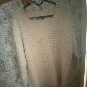 Vit stickad v-ringad tröja - Mysig vit stickad tröja med v-ringning och grovstickat mönster. Perfekt för kyliga dagar och enkel att matcha med olika outfits. Långa ärmar och avslappnad passform.