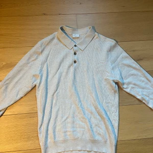 Beige pikétröja från John Henric - Säljer en stilren beige pikétröja från John Henric i storlek L. Tröjan har lång ärm, klassisk krage och knappar framtill. Materialet är strukturerat och känns mjukt mot huden. Perfekt för en avslappnad men snygg look.