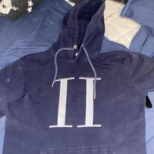 Mörkblå hoodie från Les Deux - Säljer en mörkblå hoodie från Les Deux i storlek M. Tröjan har en stor vit logga på bröstet och klassisk huva med dragsko. Perfekt för en avslappnad och stilren look.