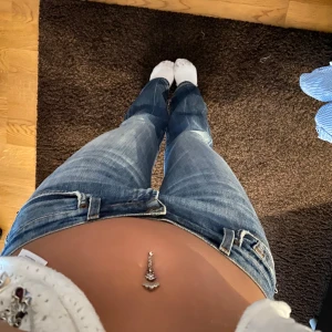 Blå bootcut jeans - Säljer ett par klassiska blå bootcut jeans med låg midja och lätt slitna detaljer. Jeansen har fem fickor, dragkedja och knapp framtill. Uppsprättade längst ner