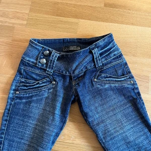 Low waist bootcut jeans 🫶🏻 - Säljer ett par blå jeans från LS Special med dubbla dekorativa knappar i midjan och snygga detaljer vid fickorna. Jeansen har låg midja och raka ben, samt klassisk denimlook med kontrastsömmar.dom är ganska små 